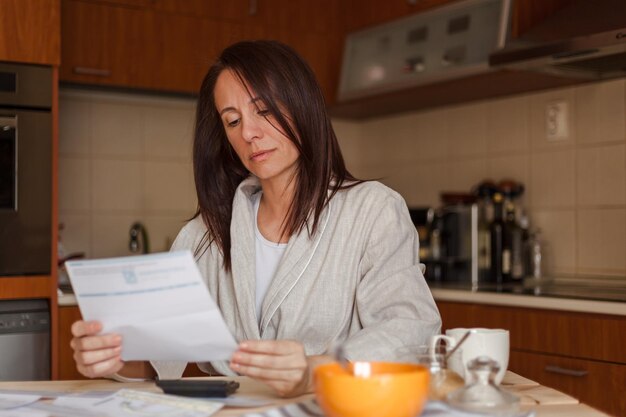 Foto mulher lendo um documento enquanto toma o pequeno-almoço em casa