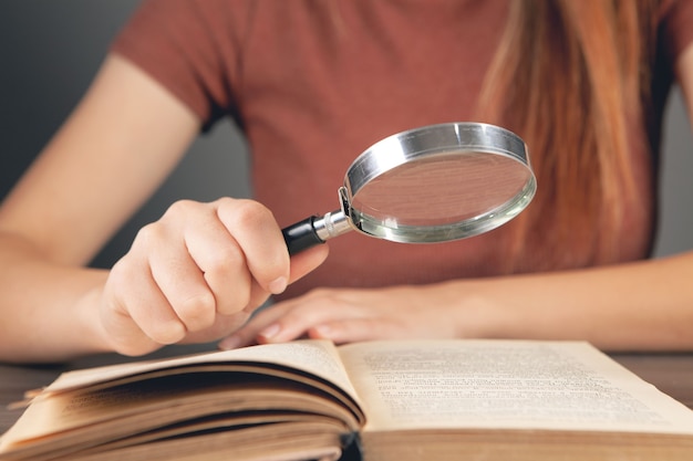 Mulher lendo um livro à mesa com uma lupa