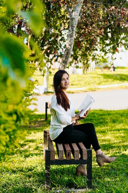 Mulher lendo um livro em um banco do parque