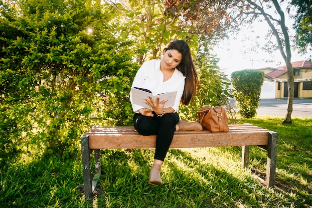Mulher lendo um livro em um banco do parque