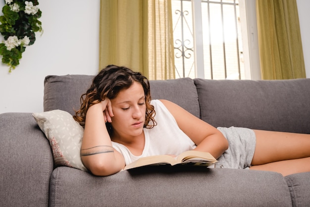 Mulher lendo um livro na sala de estar sentada no sofá