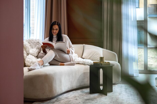 Foto mulher lendo um livro sentada no sofá em casa