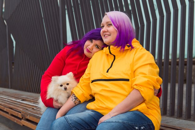 Mulher lésbica com cabelo de duas cores sentada em um banco ao ar livre segurando um spitz fofo de cachorro