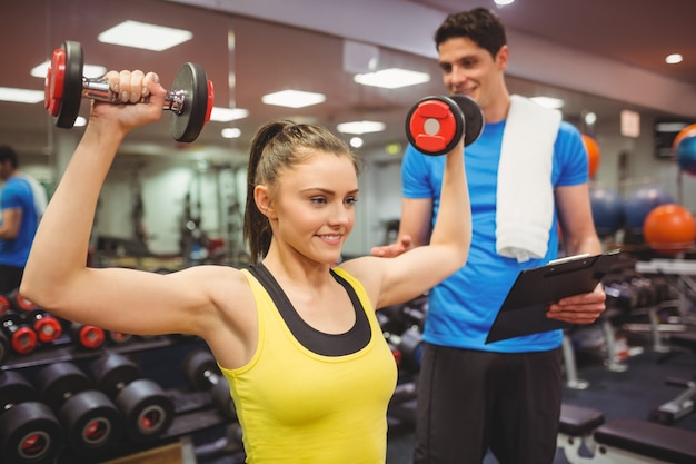 Mulher levantando dumbbells com seu treinador