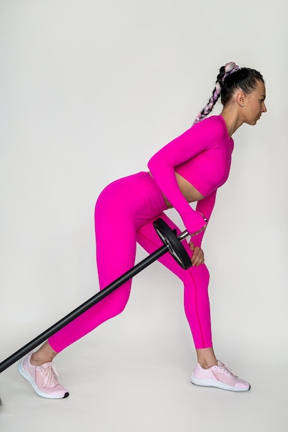 Foto mulher levantando uma barra trabalhando em um ginásio contra um fundo de parede branca monocromática