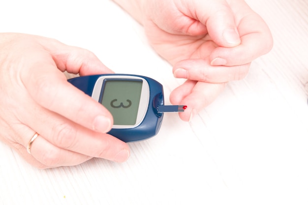 Mulher levantou um dedo com uma gota de sangue para medir o açúcar no sangue em um medidor de glicose, conceito de diabetes