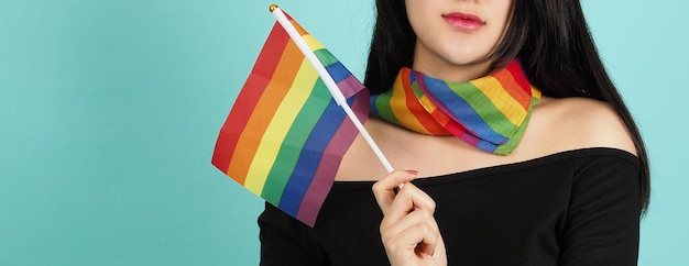 Mulher LGBTQ segurando a bandeira do orgulho em pé contra um fundo verde azul