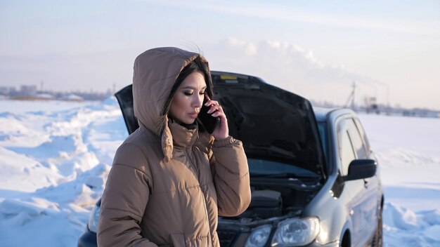 Mulher liga para o serviço de assistência automóvel perto de um automóvel avariado