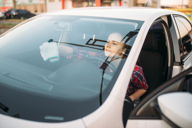 Mulher limpa o para-brisa do carro por dentro