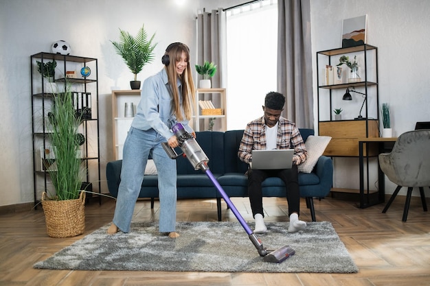 Foto mulher limpando a casa enquanto homem trabalhando no laptop
