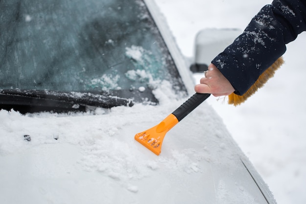 Mulher limpando a neve do carro no inverno