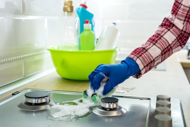 Mulher limpando a superfície do gás de aço inoxidável na cozinha com luvas de borracha.