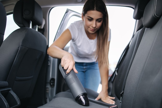 Mulher limpando o banco de trás em seu carro na garagem em casa, mulher usando aspirador de pó portátil para