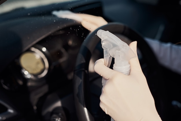 Mulher limpando o painel do carro com spray de desinfecção para proteger do coronavírus. lavagem de carro