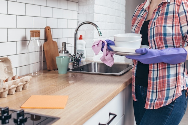 Mulher limpando pratos com toalha na cozinha.