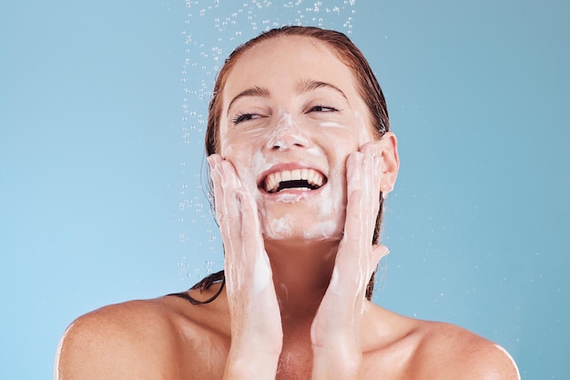 Mulher limpando rosto e sabonete com banho de beleza e higiene com aliciamento isolado em fundo azul Sustentabilidade do modelo feminino e gota d'água com felicidade dermatologia e cuidados com a pele em estúdio