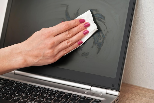 Mulher limpando tela de notebook com lenço branco, detalhe nos dedos segurando toalha de papel.