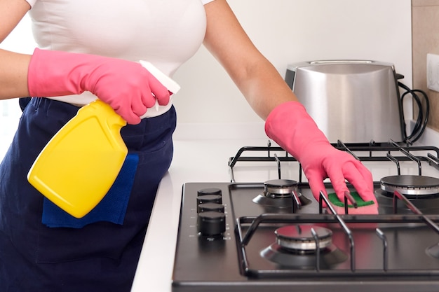 Mulher limpando um fogão a gás com utensílios de cozinha