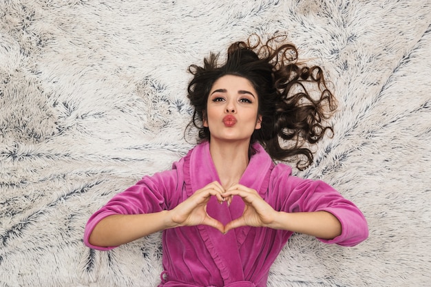 Mulher linda com cabelo longo encaracolado, vestindo um roupão feminino deitada sobre pelo branco em apartamento