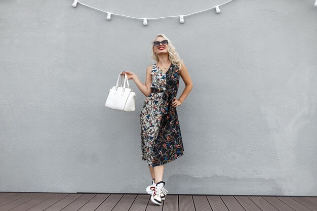 Mulher linda e feliz com uma bolsa estilosa em um vestido vintage perto da parede cinza