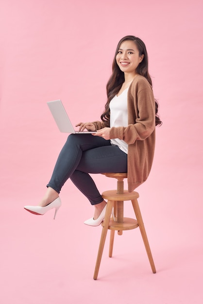 Mulher linda e feliz trabalhando com um laptop, isolada sobre fundo rosa