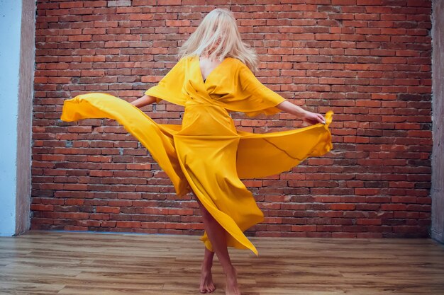 Mulher linda em um vestido amarelo contra uma parede de tijolos