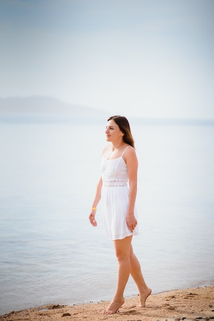 Mulher linda em um vestido branco, caminhando na praia.