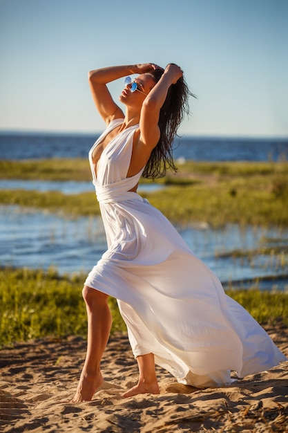 Mulher linda em um vestido branco posando na costa da baía em um dia ensolarado de verão