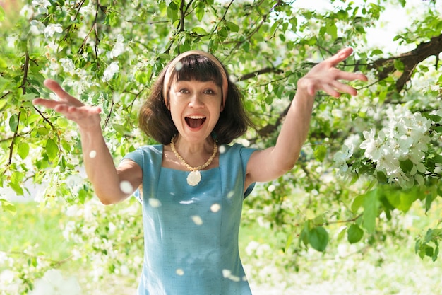 Mulher linda em um vestido longo azul com macieiras florescendo no jardim primavera, ela joga pétalas de flores