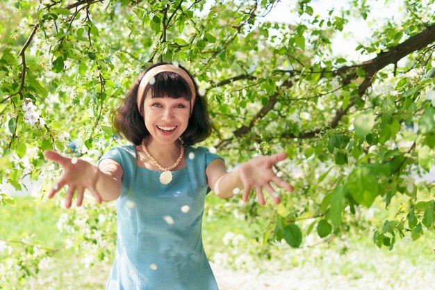 Mulher linda em um vestido longo azul com macieiras florescendo no jardim primavera, ela joga pétalas de flores