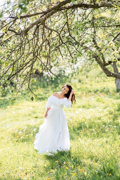 Mulher linda em um vestido longo branco em um jardim primavera. Uma garota corre por um jardim florido.