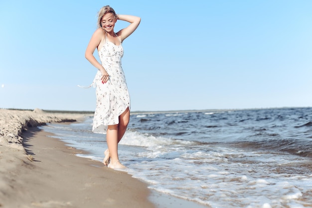 Mulher linda loira feliz se divertindo na praia do oceano enquanto dançava nas ondas.