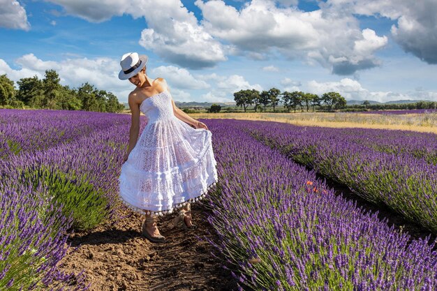Mulher linda posando em um campo de lavanda em flor com seu vestido branco e chapéu