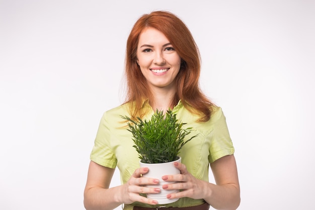 Mulher linda ruiva segurando um vaso com uma planta no fundo branco