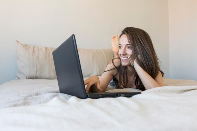 Mulher linda sorridente usando telefone celular na cama em casa