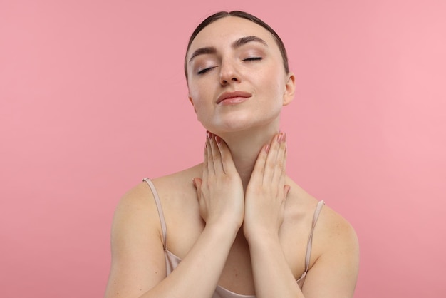 Mulher linda tocando seu pescoço em fundo rosa