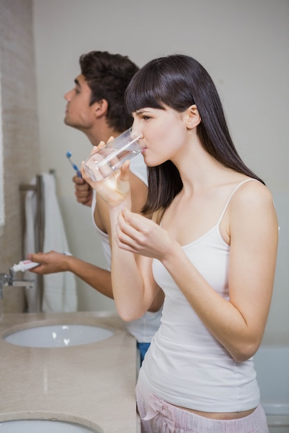 Mulher linda tomando um copo de água com medicina e homem escovando os dentes