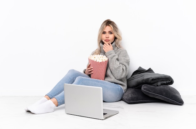 Mulher loira adolescente comendo pipoca enquanto assiste a um filme no pensamento laptop