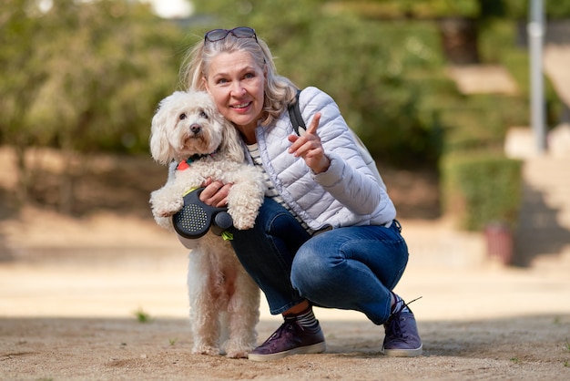 Mulher loira adulta andando com cachorro branco fofo na cidade de verão.