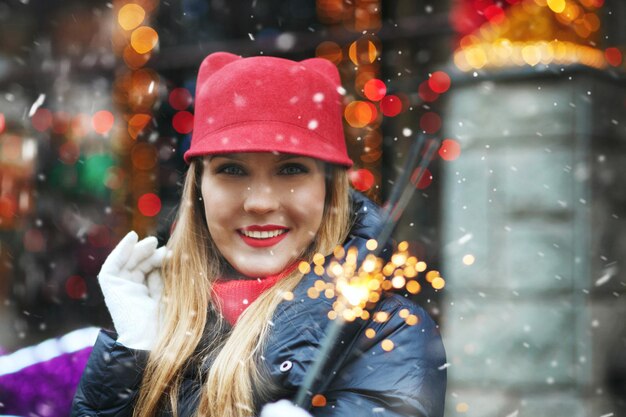 Foto mulher loira alegre usa chapéu vermelho, brincando com luzes de bengala na feira de férias. espaço para texto