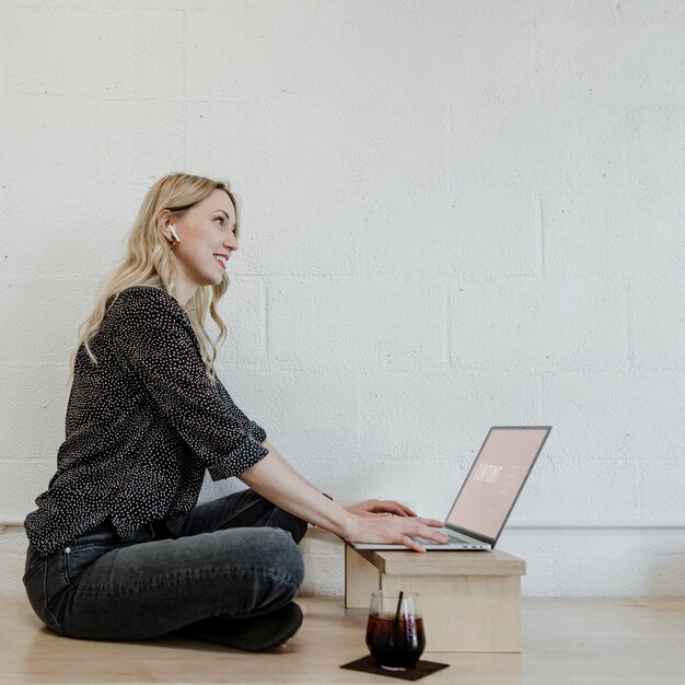 Mulher loira alegre usando um laptop em um piso de madeira