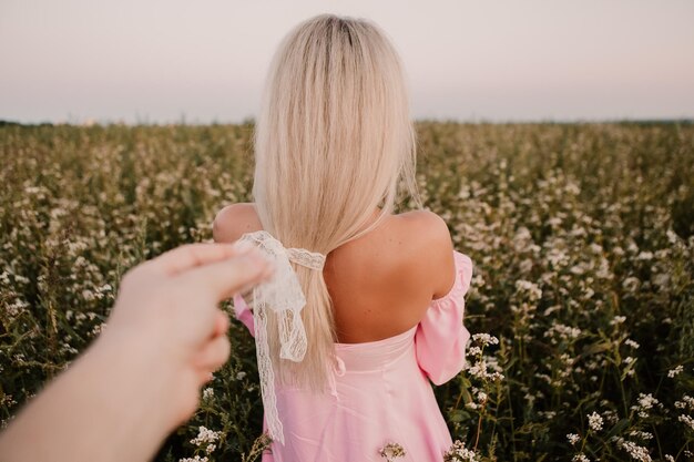 Mulher loira andando no grande campo infinito de margaridas em noite de verão. Senhora usa vestido rosa
