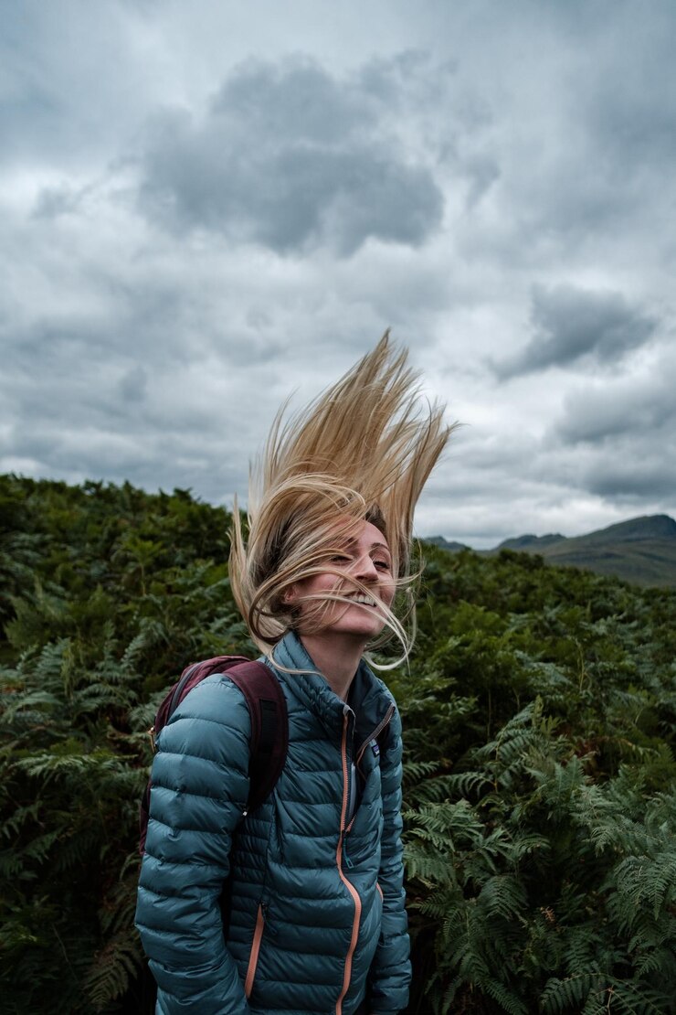 Foto mulher loira batendo o cabelo na frente de um campo de samambaias
