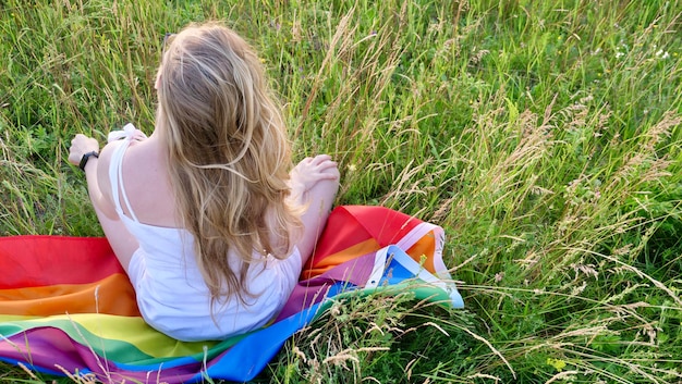 Mulher loira bissexual lésbica sentada na bandeira LGBT na grama em vestido branco Apoio à orientação não tradicional no mês da dignidade o dia da bissexualidade