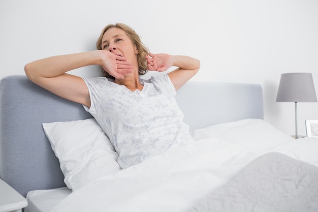 Mulher loira bocejando e esticando na cama pela manhã