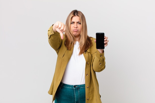 Mulher loira bonita e curvilínea se sentindo mal, mostrando os polegares para baixo e segurando um telefone inteligente