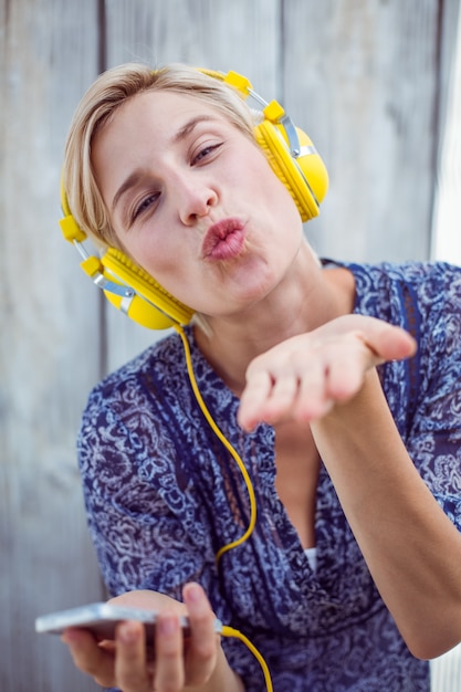 Mulher loira bonita ouvindo música com seu celular e soprando beijo