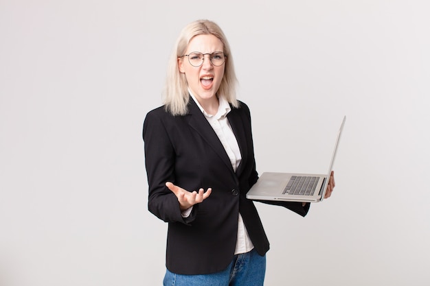 Mulher loira bonita parecendo zangada, irritada e frustrada segurando um laptop