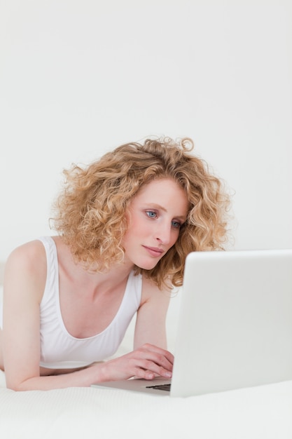 Mulher loira bonita relaxante com o laptop dela enquanto estava deitado na cama dela