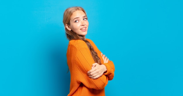 Mulher loira bonita sorrindo alegremente, sentindo-se feliz, satisfeita e relaxada, com os braços cruzados e olhando para o lado